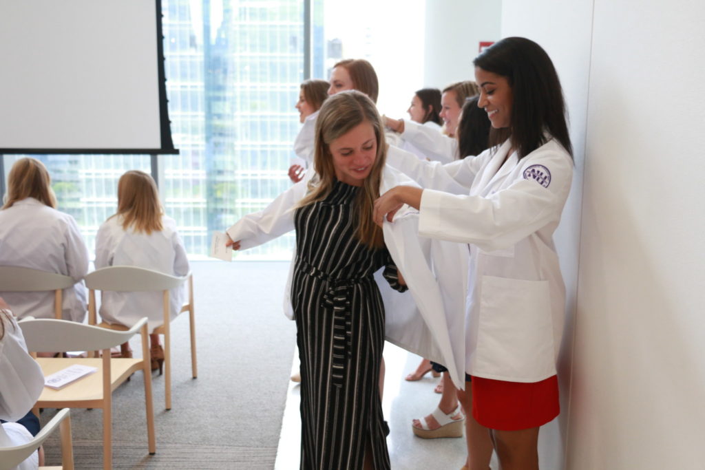 Before receiving their program patch, students are helped into their white coats.