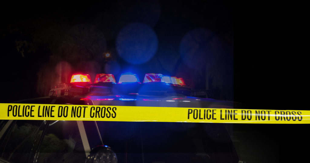 A photograph of a police car and yellow police tape.