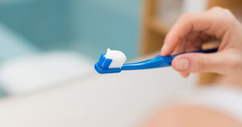 Common Antimicrobial May Raise Risk of Colon Disease Woman hand holding toothbrush with toothpaste applied on it in bathroom. Close up of female hand ready for brushing teeth. Young woman hand holding a blue toothbrush with white tooth paste.