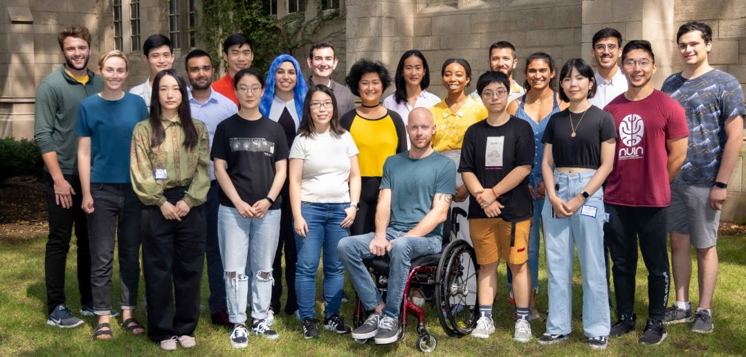 The entering NUIN PhD program poses in a group on grass in front of a Northwestern building